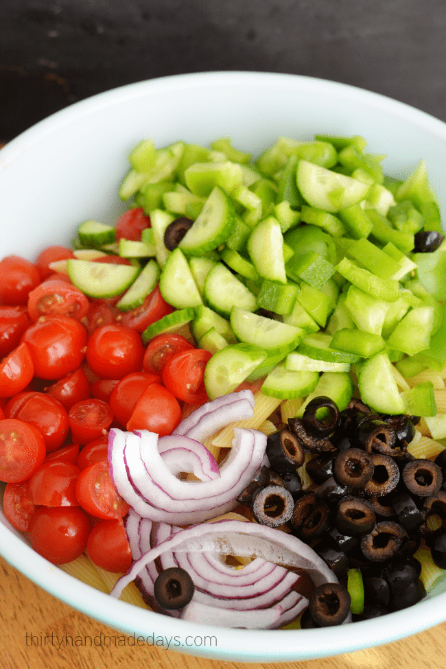 Add vegetables to pasta for greek pasta salad