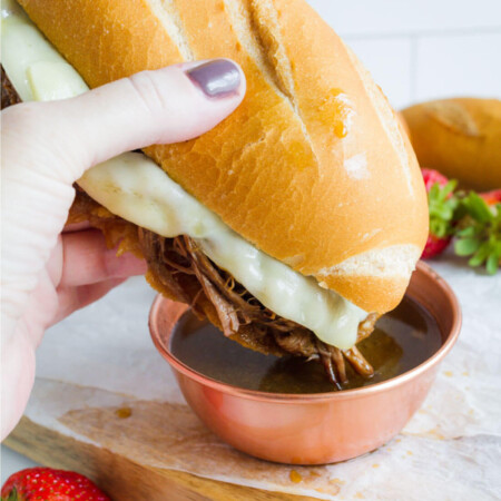 Dipping French Dip sandwiches into au jus sauce.