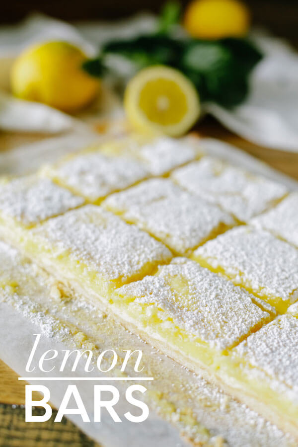 Lemon bars up close with lemons in the background